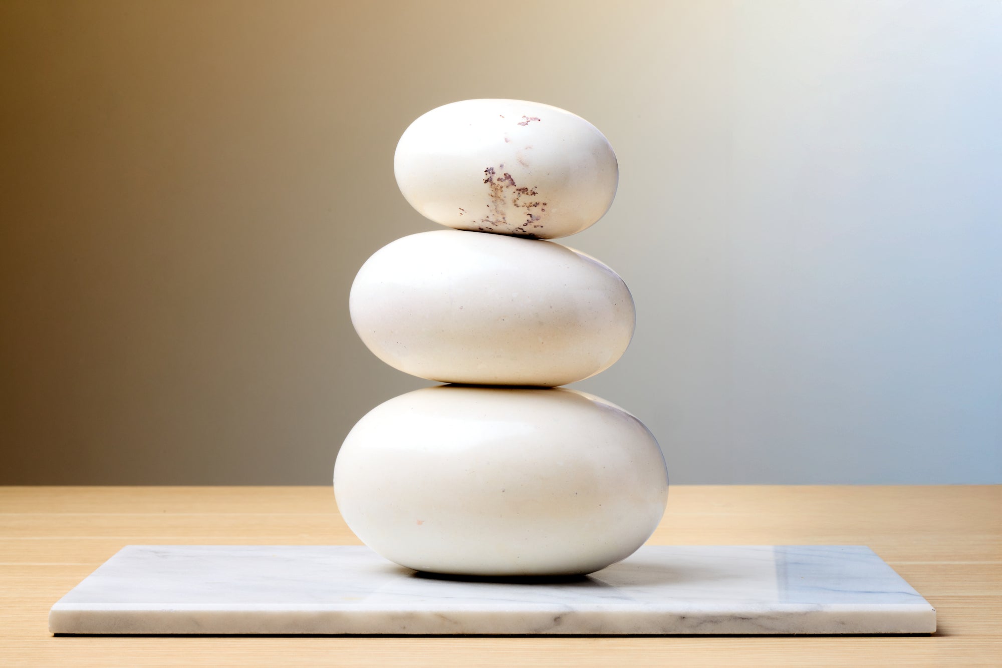 Stack of three white stones on a marble slab with a gradient background