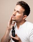 Man holding a blue oil bottle with a dropper, possibly a skincare product, against a beige background