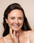 Woman smiling and touching her face against a beige background with Geri G. products