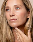 Close-up of a woman with long blonde hair touching her face against a neutral background