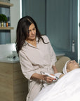 Woman in a robe attending to another person lying on a bed in a clinical setting.