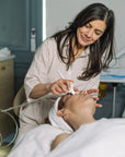 Woman performing a facial treatment on another woman in a clinical setting at Geri G. Beauty.