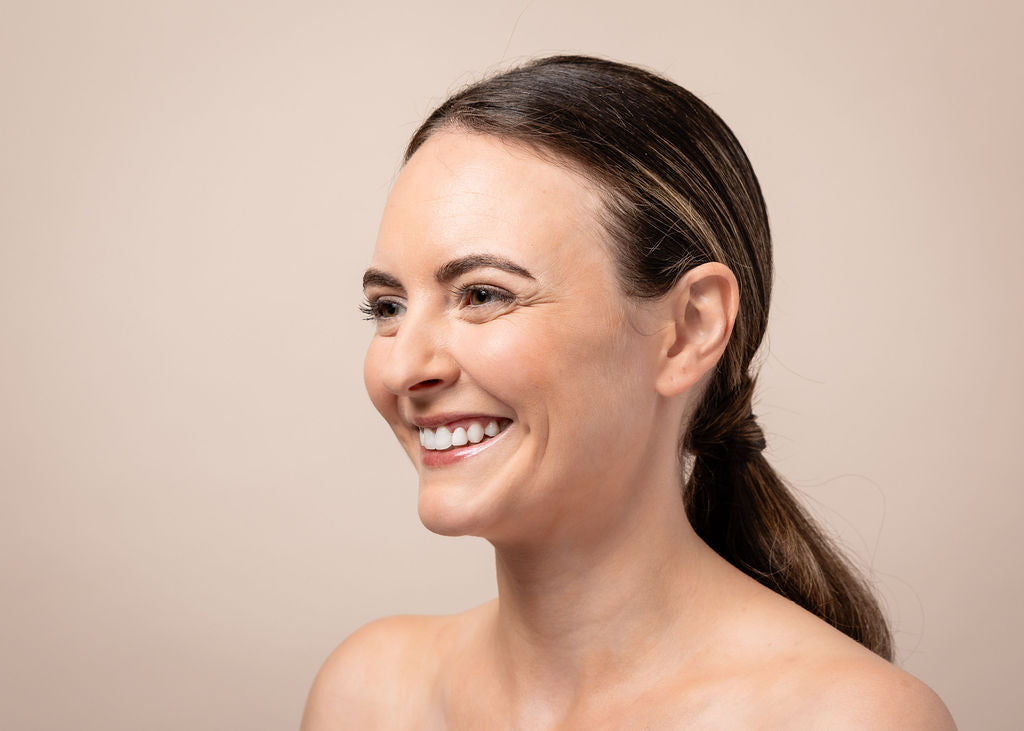 Woman with a ponytail smiling against a beige background