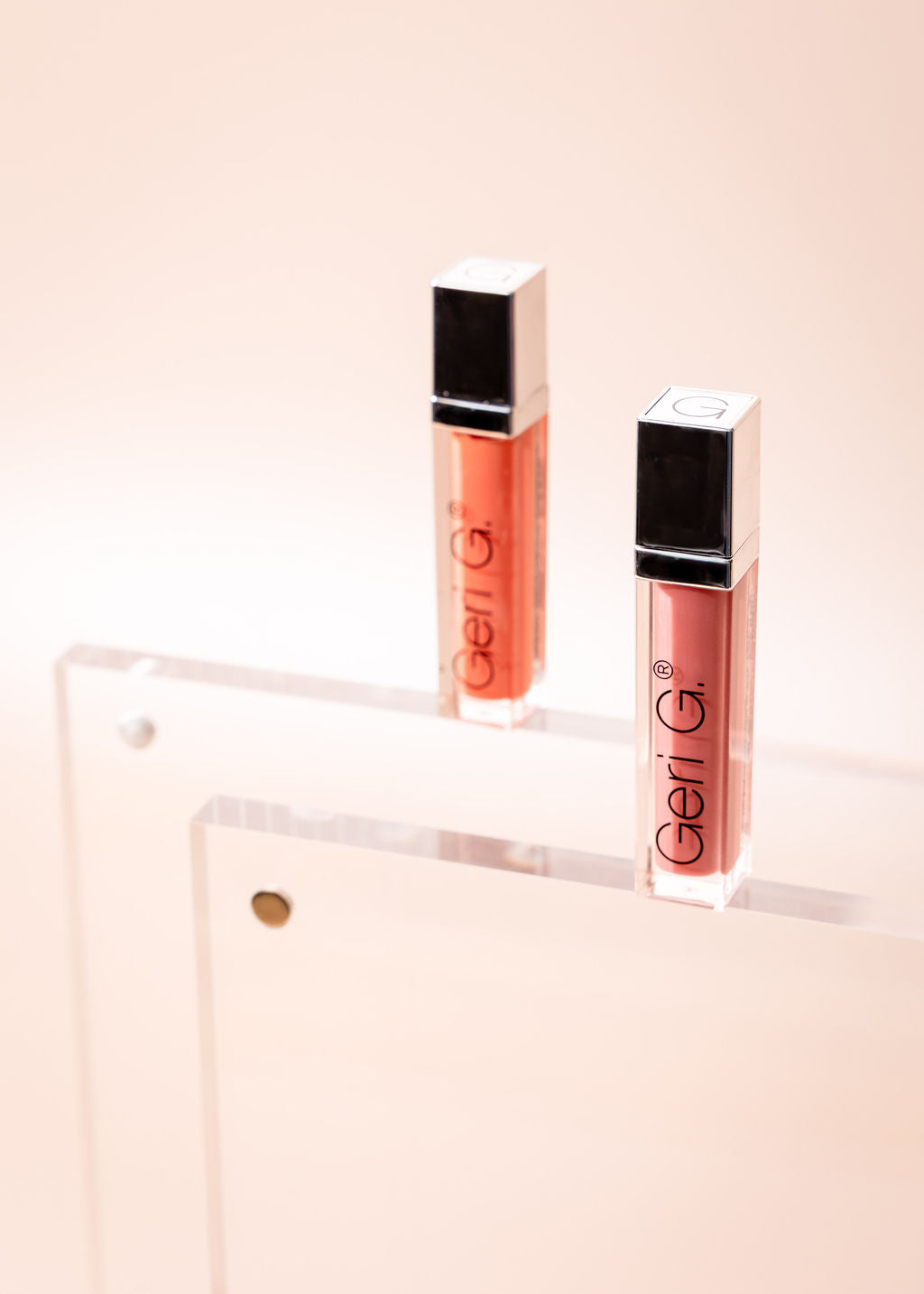Two lip glosses with 'Geli G' branding on a light pink background
